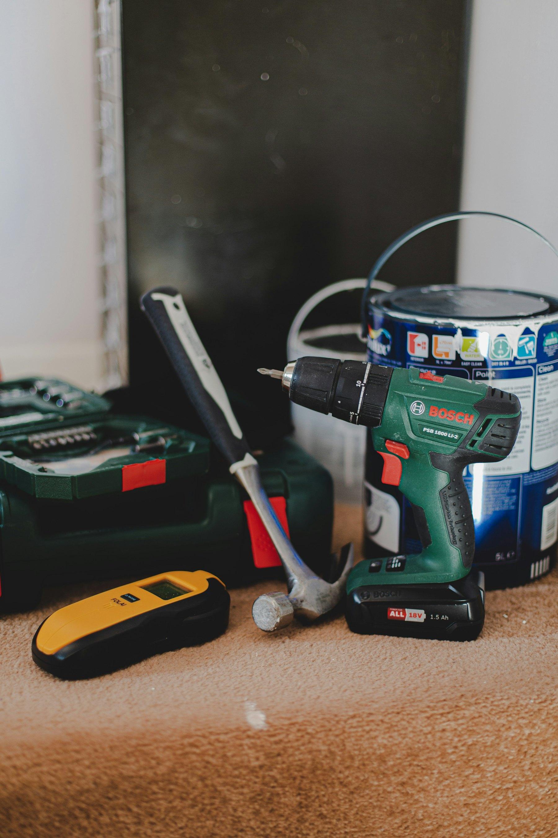Drill, hammer, stud finder and paint can on the floor