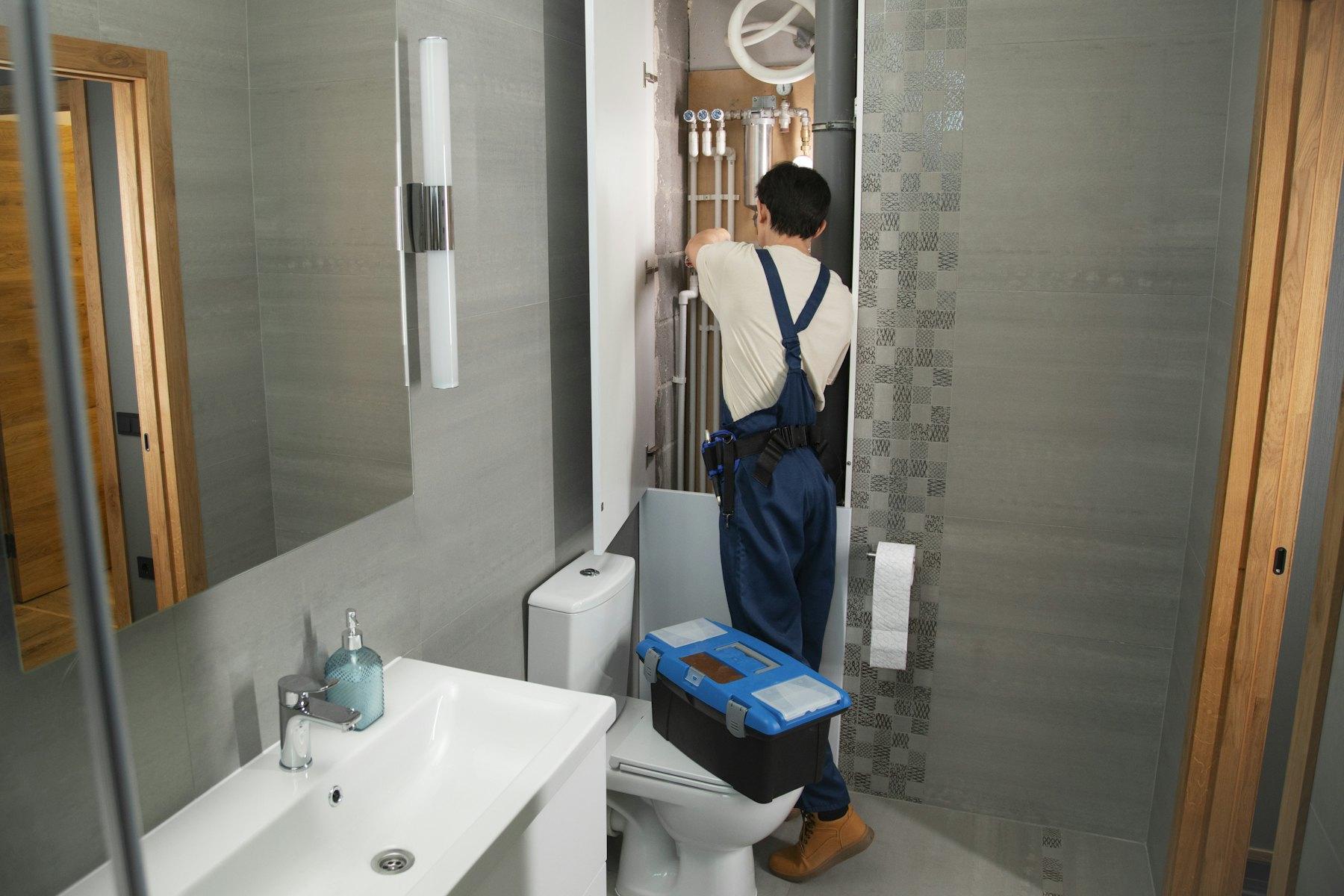 Plumber with toolbox working in a commercial restroom